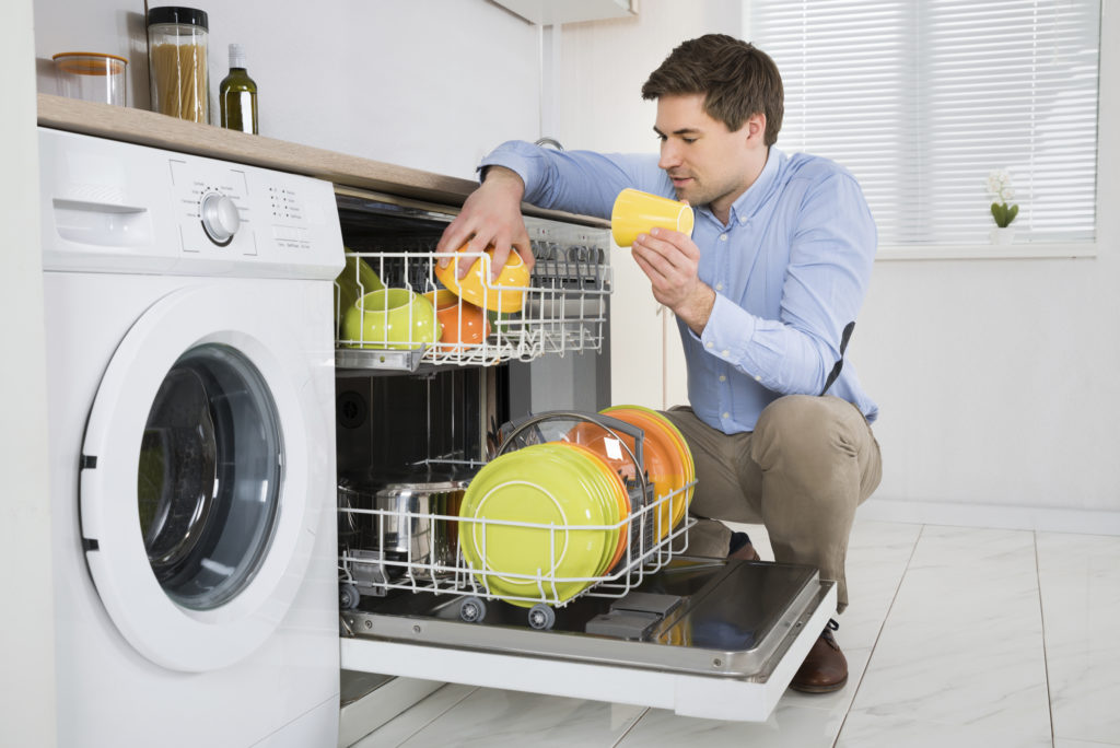 Young Happy Man Arranging Dishes In Dishwasher In Modern Kitchen